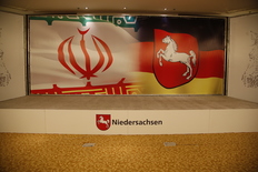 Eine leere Bühne mit dem Niedersachsen-Logo, im Hintergrund links die iranische Flagge und rechts die deutsche Flagge