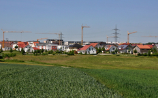 Neubaugebiet mit Häusern und Baukränen im Hintergrund und Feld im Vordergrund