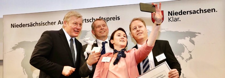 Wirtschaftsminister Althusmann, links mit einem Mann und einer Frau, die Frau macht ein Selfie mit dem Smartphone, im Hintergrund ist eine Pressewand mit der Aufschrift "Niedersächsischer Außenwirtschaftspreis" und "Niedersachsen.Klar&qu