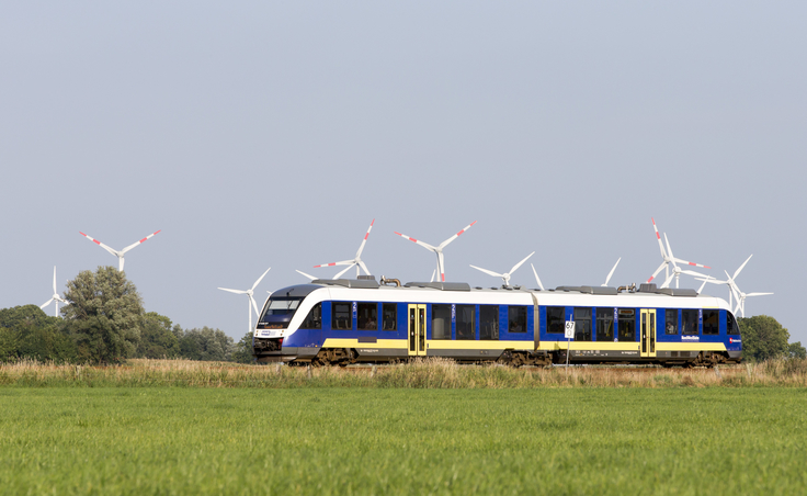 Blau-gelber Zug, im Hintergrund Windräder