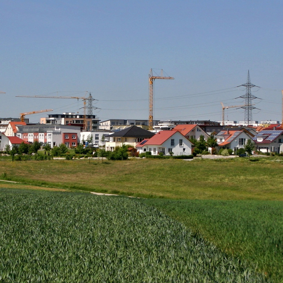 Neubaugebiet mit Häusern und Baukränen im Hintergrund und Feld im Vordergrund